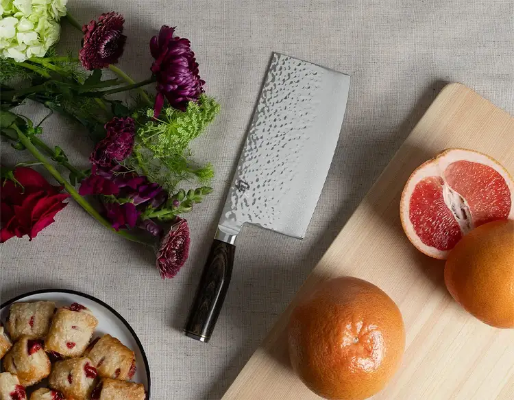 A Premier Vegetable Cleaver sits on a table between a bouquet of flowers and sliced grapefruit.