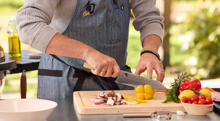 Chef slicing yellow bell pepper with a Shun Premier Blonde Kiritsuke on an outdoor prep station. Click to shop.