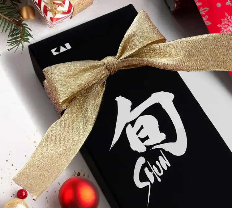 A Shun box wrapped with a bow lies on a table with festive garnishing.