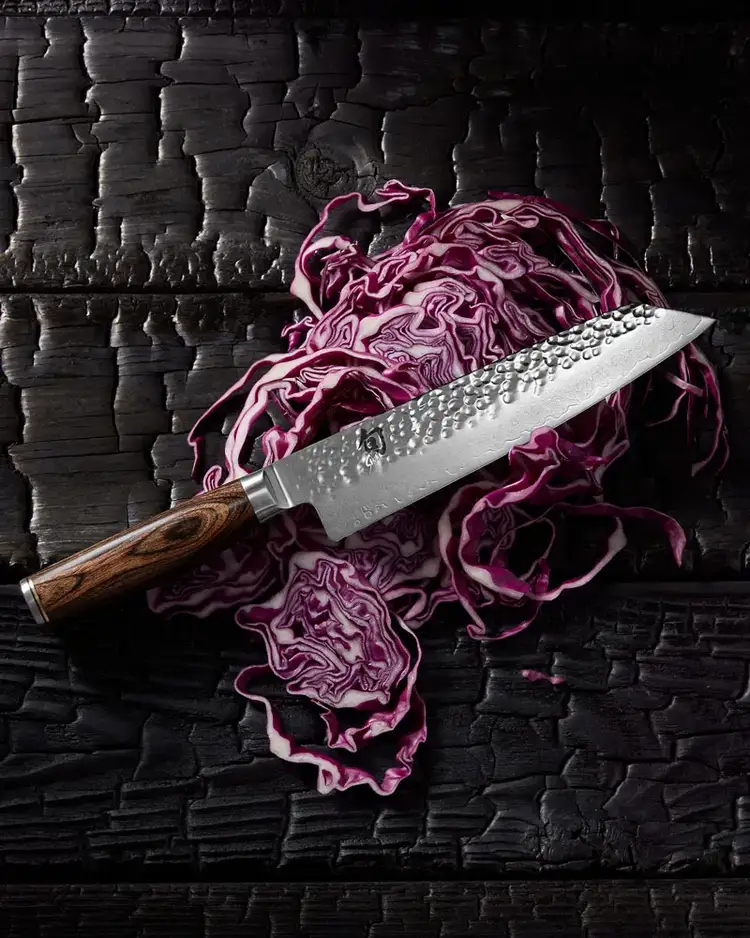 Shun Premier Kiritsuke with dark walnut handle resting on sliced red cabbage on black charred wood. Click to shop.