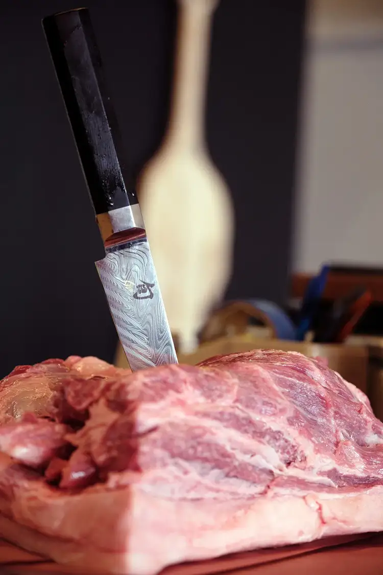 A Shun Dual Core Utility/Butchery knife stands upright while it is inserted into a large cut of meat