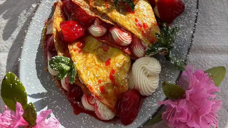 Close up of crepes filled with cheesecake mascarpone cream and covered with strawberries.