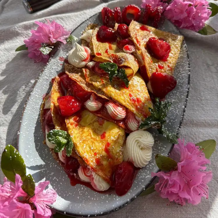 Beautifully garnished strawberry cheesecake crepes surrounded by pink flowers.