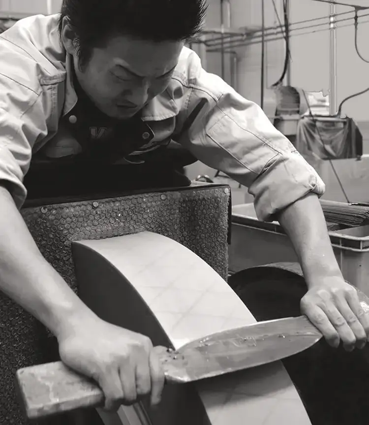 Black-and-white image of a craftsman sharpening a knife in Japan.