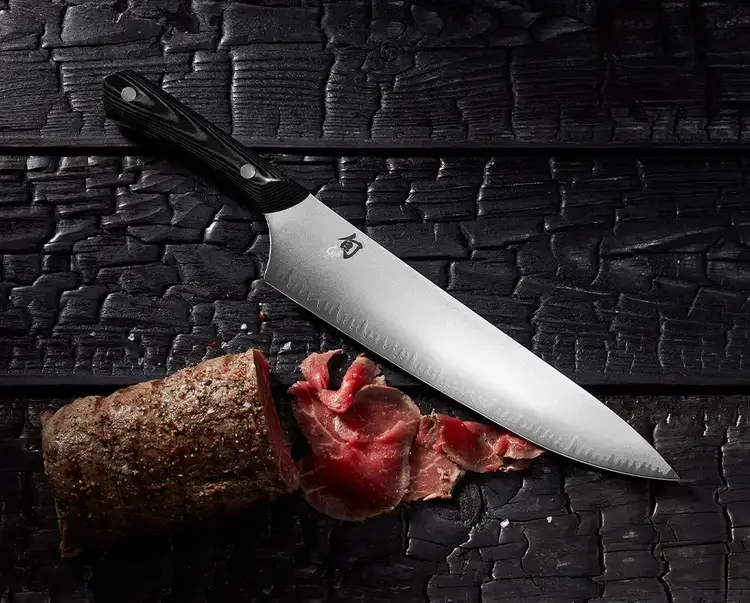 A 10" Narukami Chef's Knife lies next to thinly sliced meat.