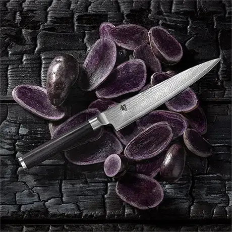 Shun Classic utility knife styled with purple potatoes on a dark textured surface.
