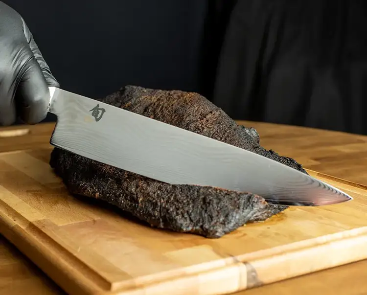 A Classic 10" Chef's Knife slices through a barbequed roast.
