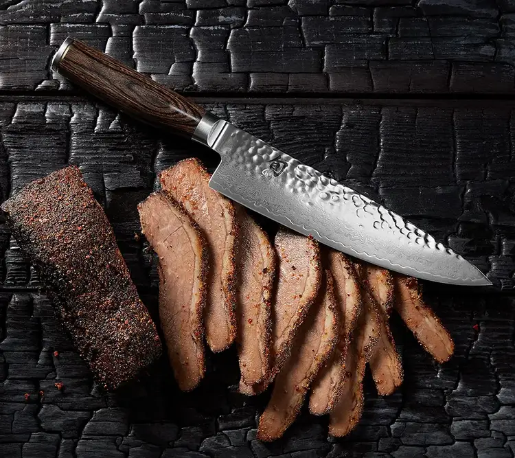 A 8" Premier Chef's Knife lying next to slices of a roast.