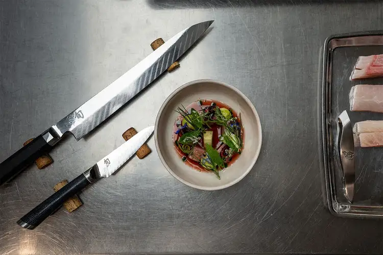 Dual Core 10.5" Yanagiba and Shiranami 4" Paring next to a prepared fish dish and a tray of fish with Fish Bone Tweezers off to the right side.