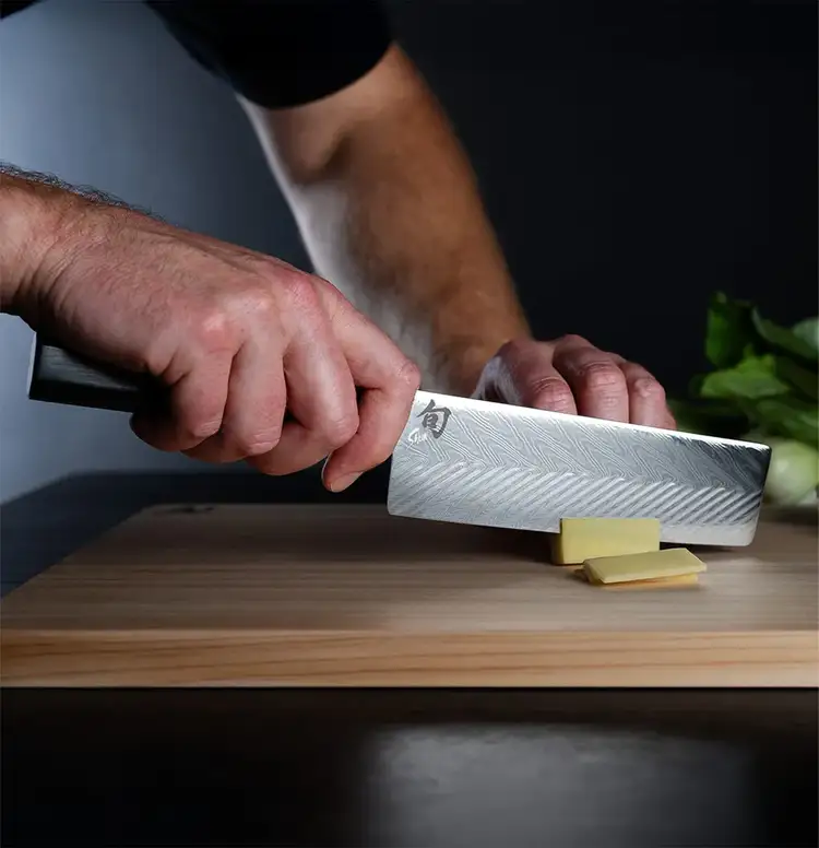 A chef slices vegetables with a Dual Core Nakiri.