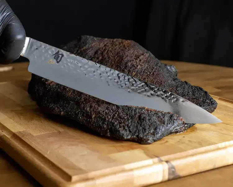 A Premier 10" Chef's Knife slices through a barbequed roast.