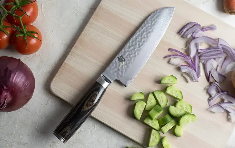 A Premier Santoku laying on a cutting board, surrounded by sliced vegetables.