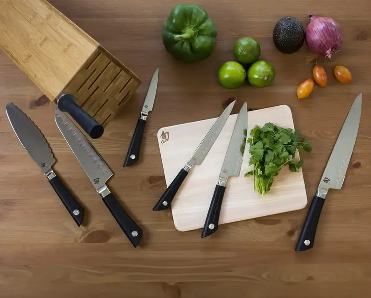A collection of Sora knives lie on a table next to a bamboo knife block.