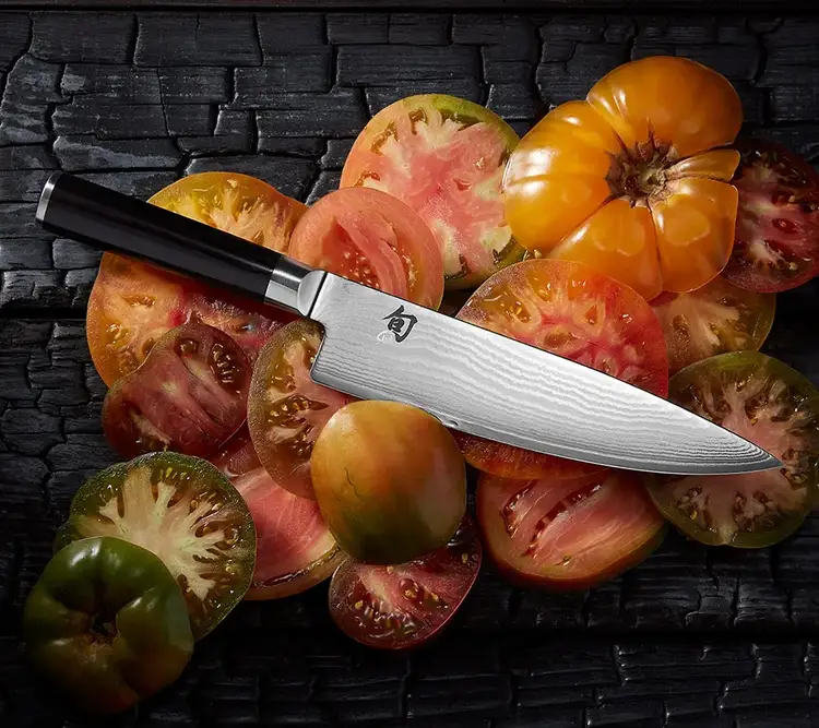 A Classic 8" Chef's Knife lies on top of thinly sliced heirloom tomatoes.