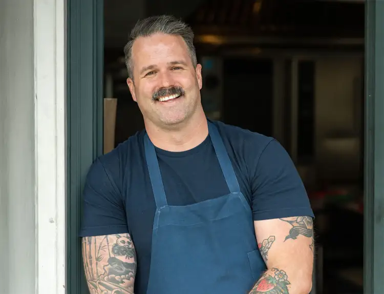 Chef Avery Hardin smiles at the camera, leaning on a doorframe.