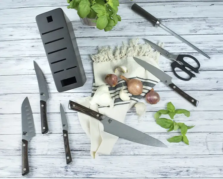 A collection of Kanso knives lie on white, slatted table.