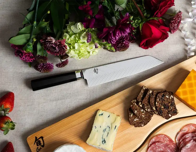 Shot of a Dual Core Kiritsuke lying next to a bunch of flowers and a cheese board.