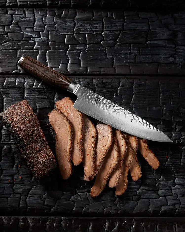 Shun Premier Chef's Knife slicing smoked brisket on a rustic wood cutting surface. Click to shop.