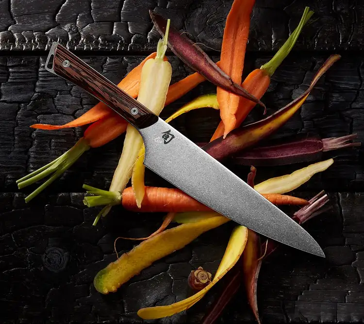 A Kanso 8" Chef's Knife rests on thin slices of colorful carrots.