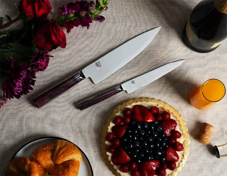 The two knives of the Kohen Knife set lie next to a fruit tart and a poured mimosa.