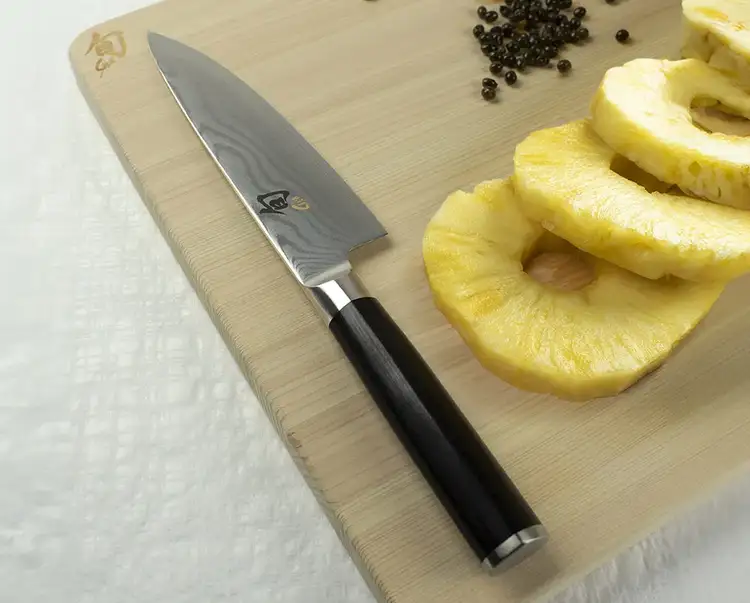 A Classic 6" Chef's Knife sits next to slices of pineapple on a hinoki cutting board.