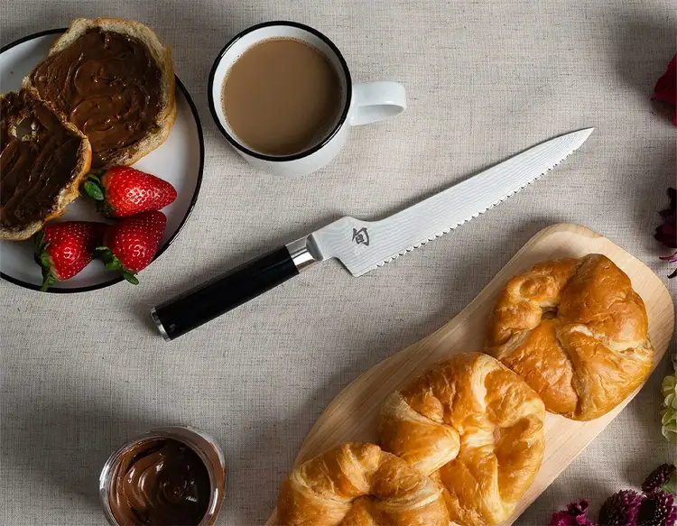 A Classic Offset Bread Knife sits between a cup of coffee and fresh croissants.